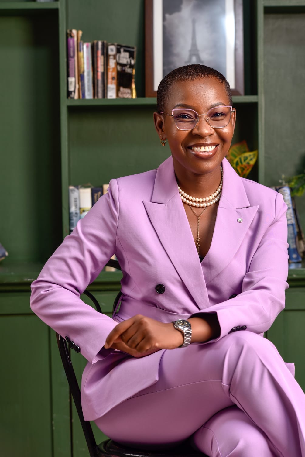 Eunice Ireri seated, in a study with green shelves